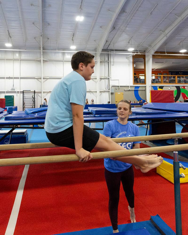 A boy working on the parallel bars with a TEG coach