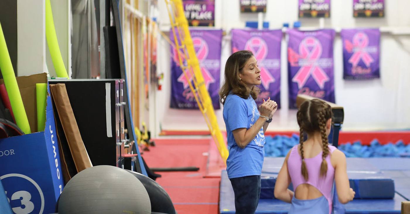 A TEG coach talking with a young gymnast at the balance beam