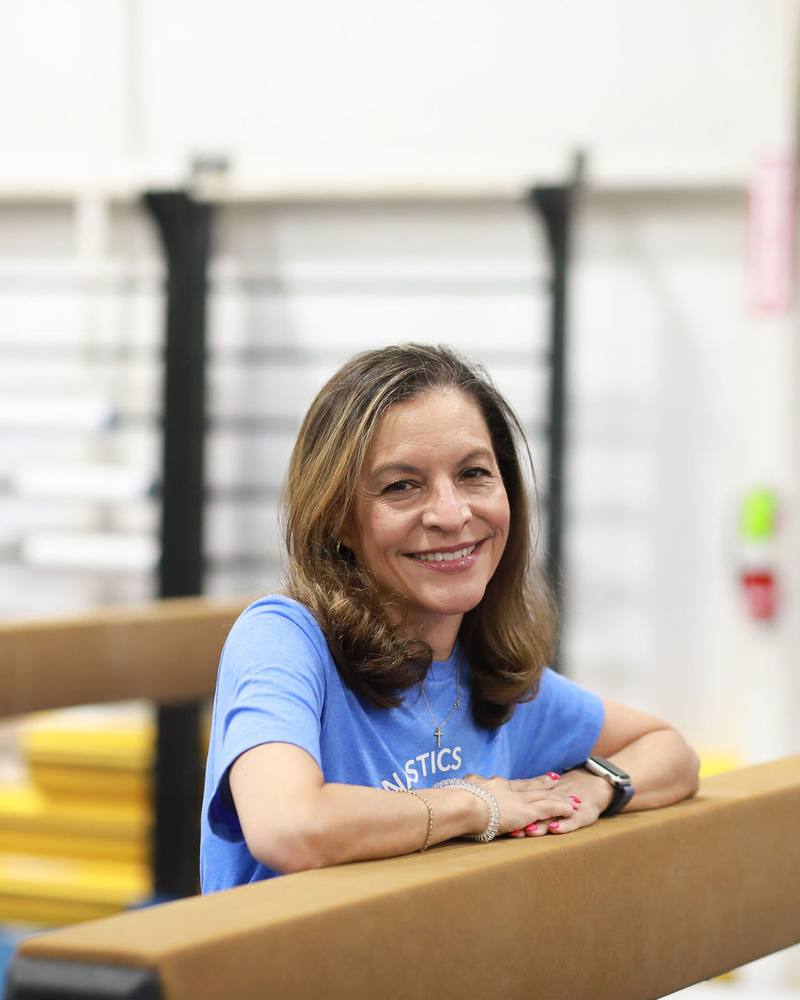 Coach Lisa Collins leaning on a balance beam in the TEG gym
