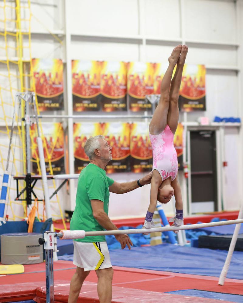 Head Coach Anatoli Toropov spotting a gymnast's handstand on the uneven bars