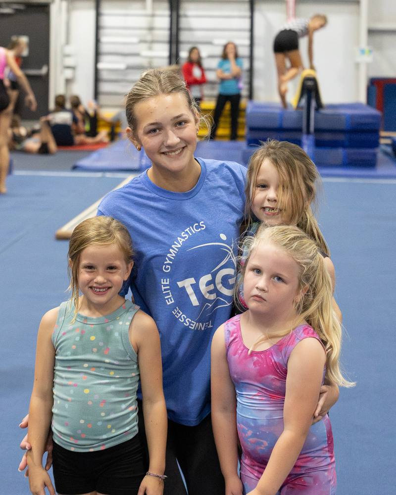 A TEG coach smiling with three young gymnasts