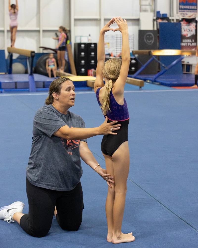A TEG coach guiding a young gymnast into a backbend