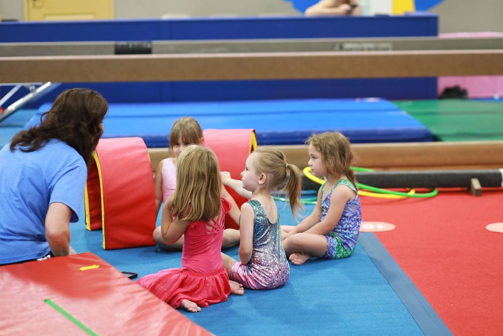 A TEG coach sitting on the mat with four preschool gymnasts during class