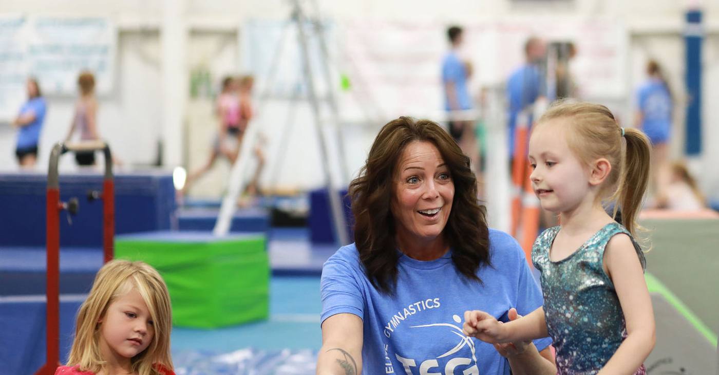 A TEG coach cheering with a young gymnast during class