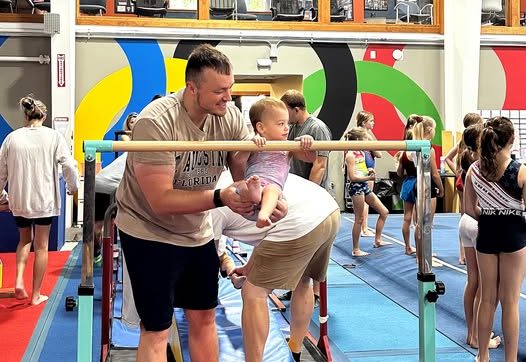 A parent helping a baby hold on to a low bar at TEG