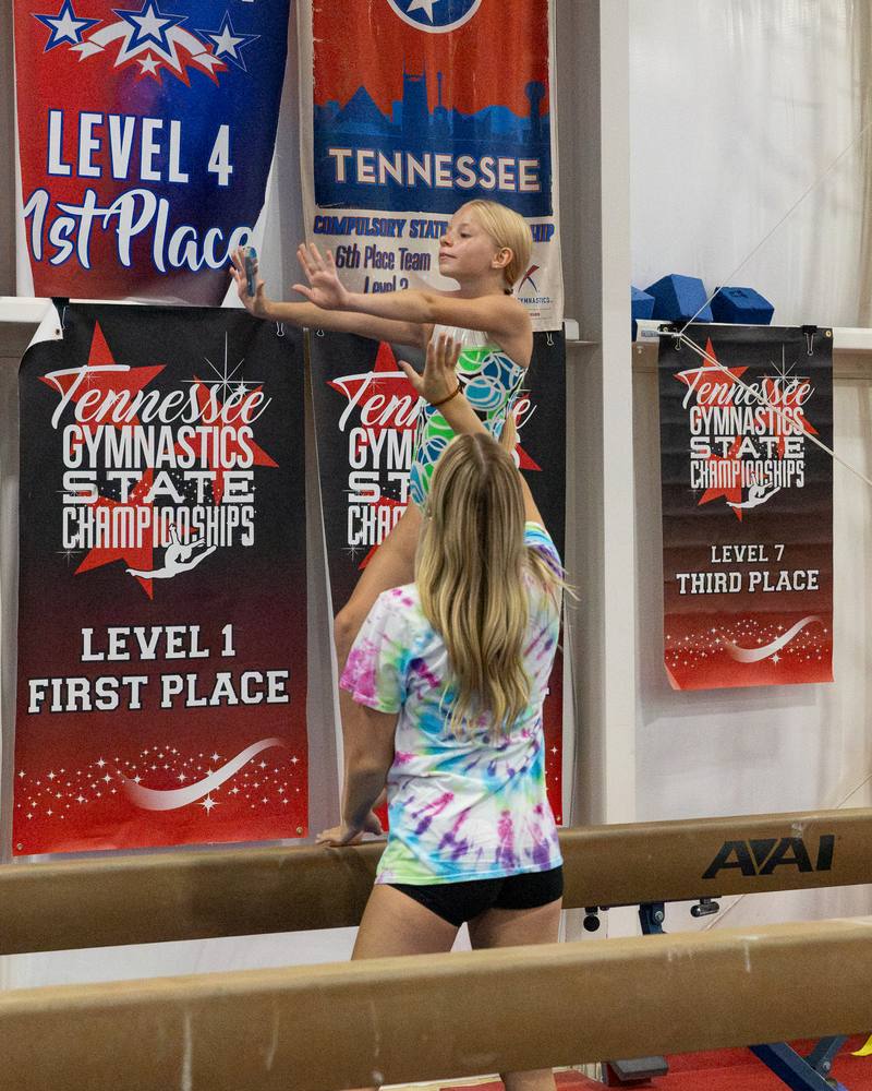 A TEG gymnast on the balance beam in front of state championship banners
